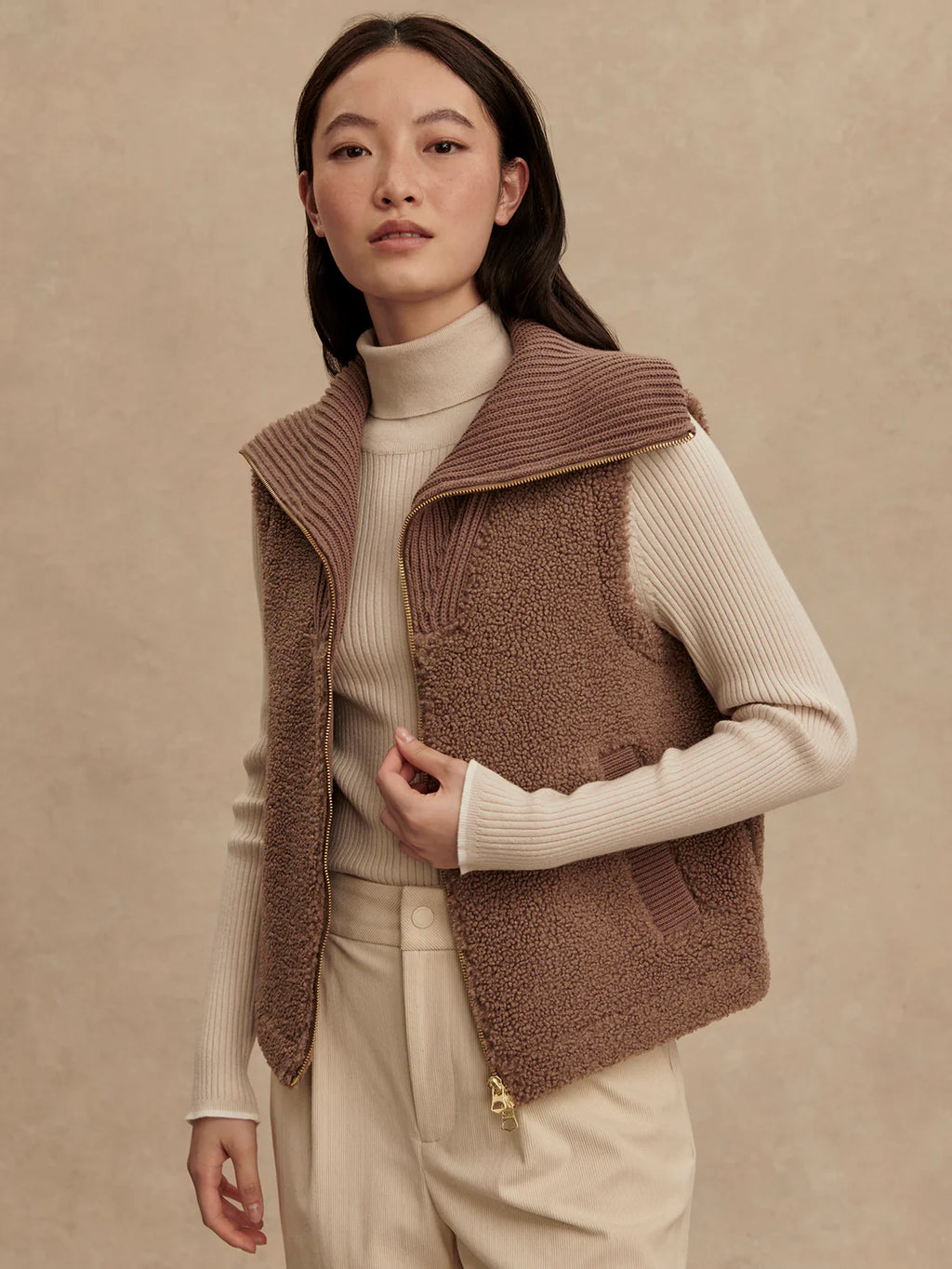 Woman wearing a brown knitted vest over a beige sweater on a beige background