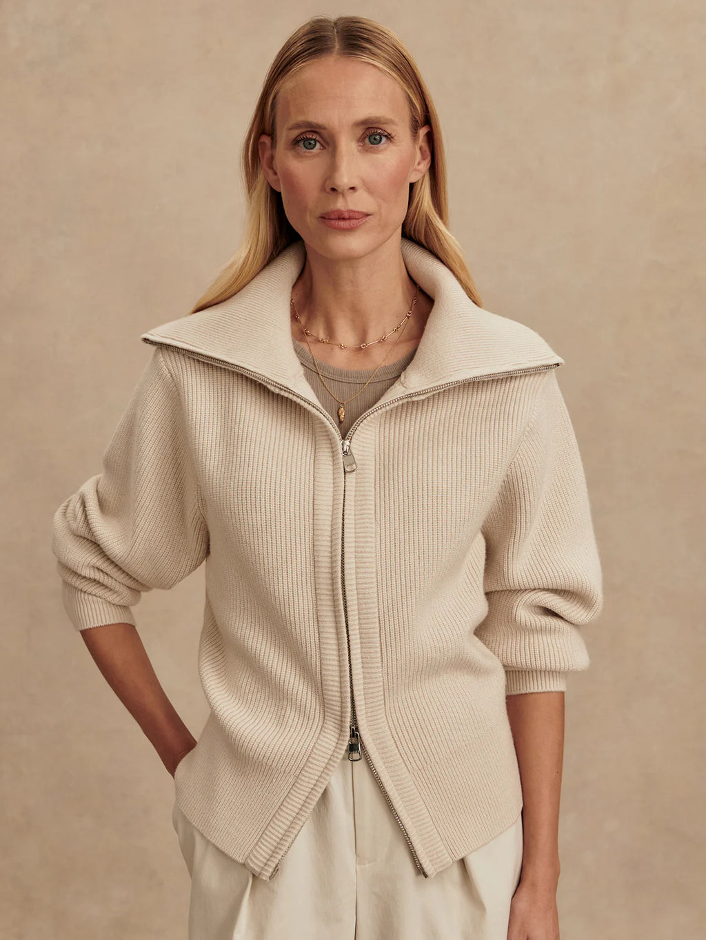Woman wearing a beige zip-up sweater against a beige background