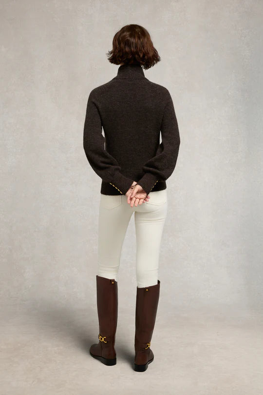 Person wearing a dark sweater, white pants, and brown boots on a neutral background