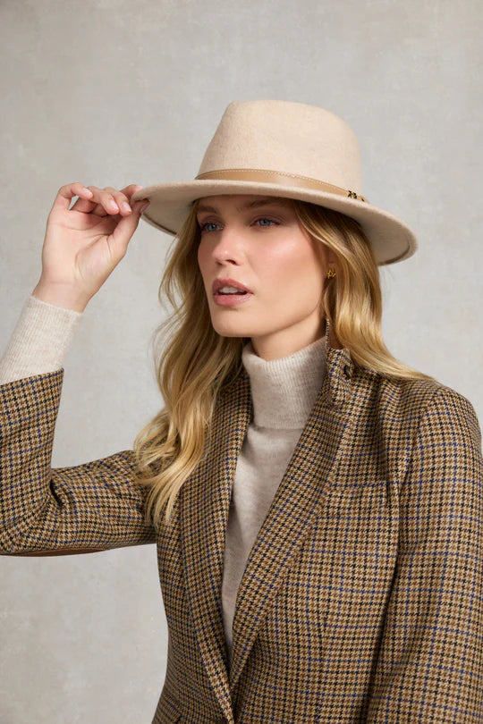 Woman wearing a beige hat and plaid blazer against a plain background