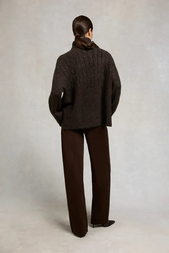 Person wearing a dark brown coat and pants against a plain background