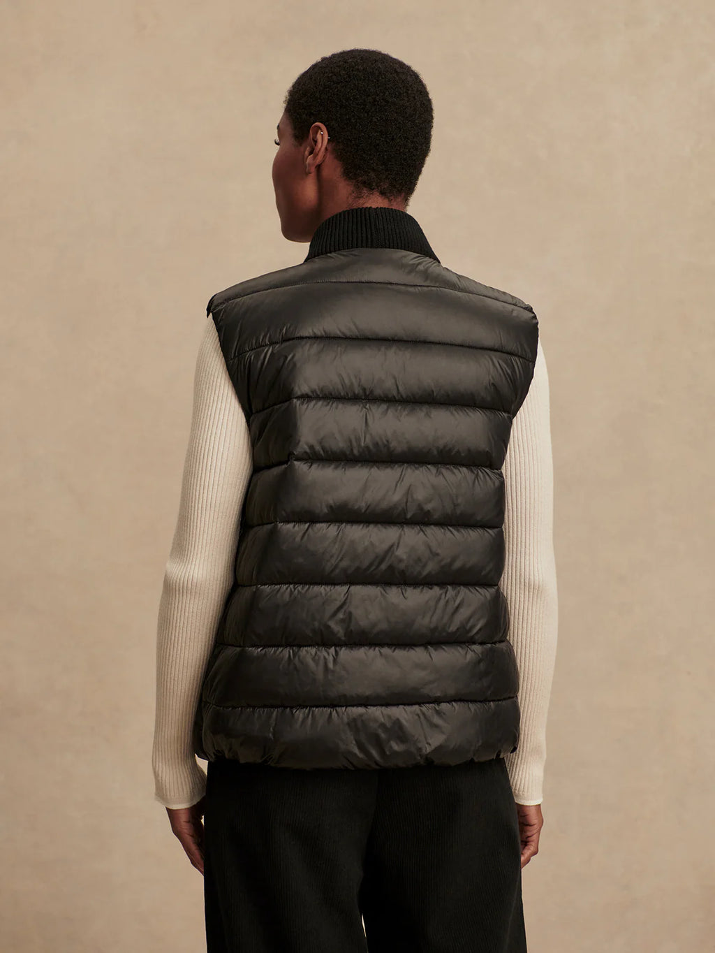 Person wearing a black puffer vest over a white shirt on a beige background