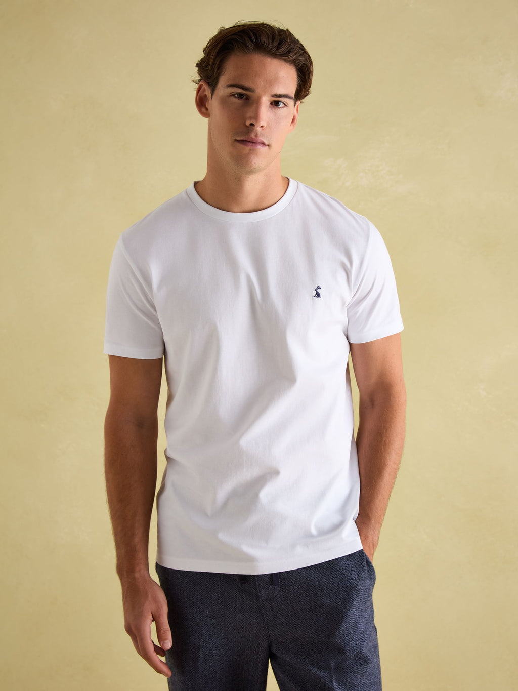 Man wearing a white t-shirt with a small logo on a beige background