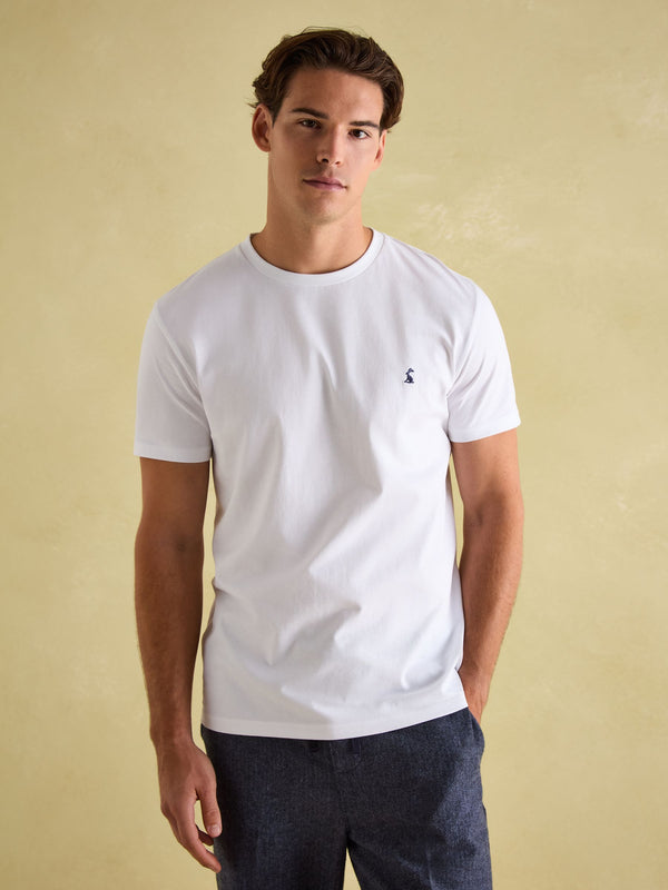 Man wearing a white t-shirt with a small logo on a beige background