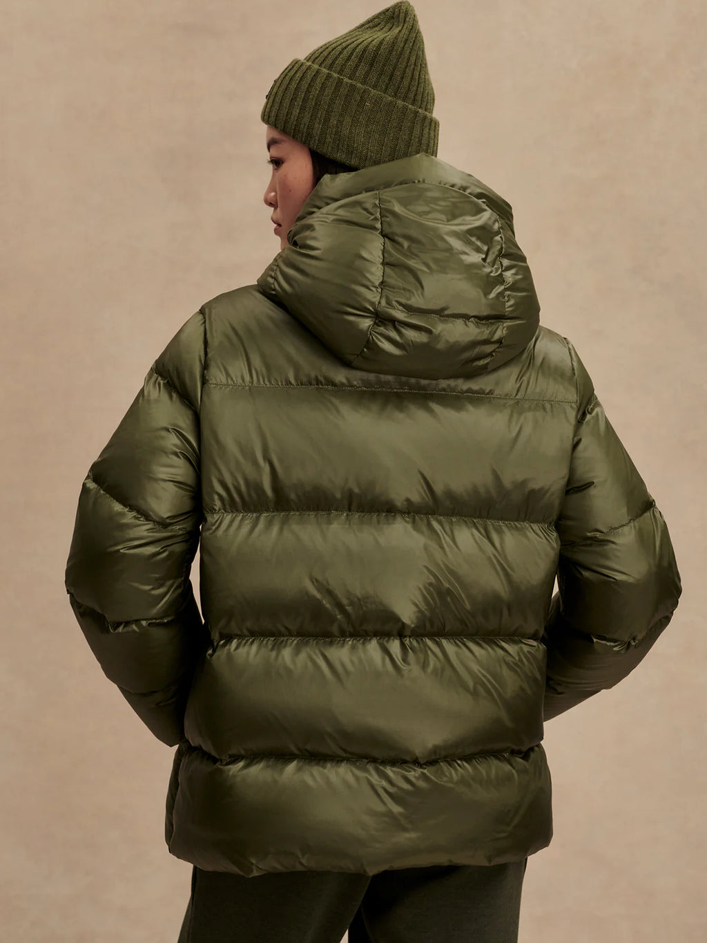 Person wearing a green puffer jacket and beanie against a beige background
