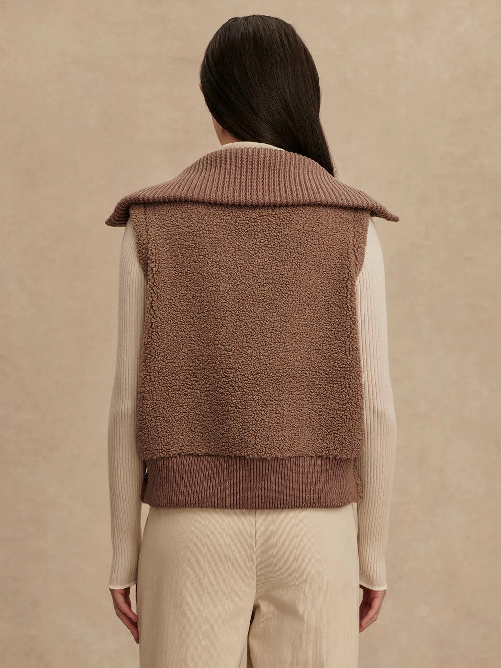 Person wearing a brown knitted vest on a beige background