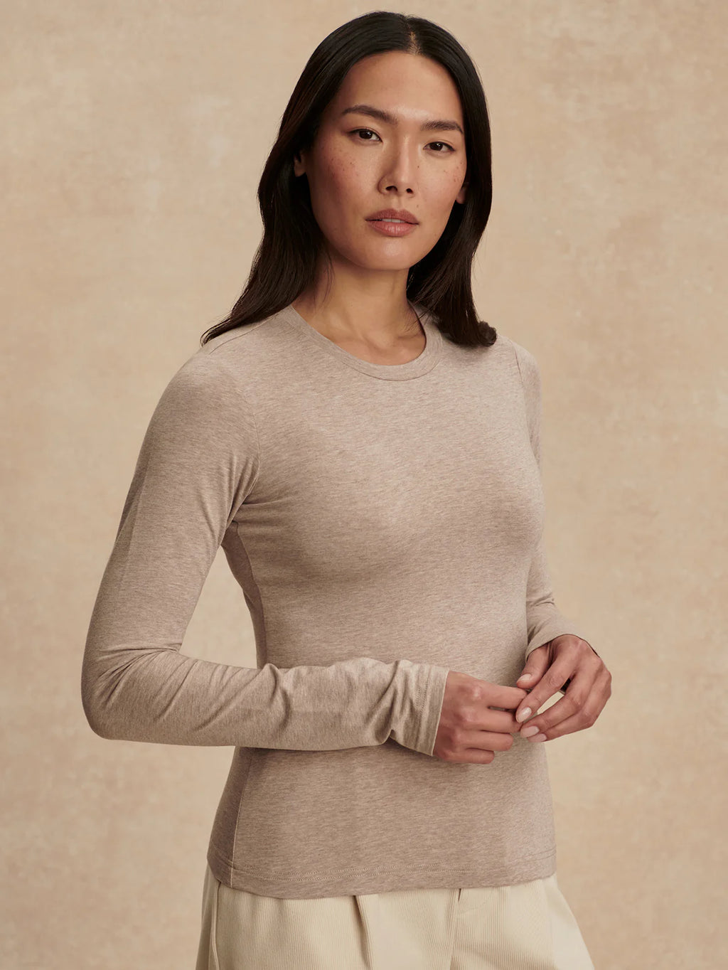 Woman wearing a beige long-sleeve top against a beige background