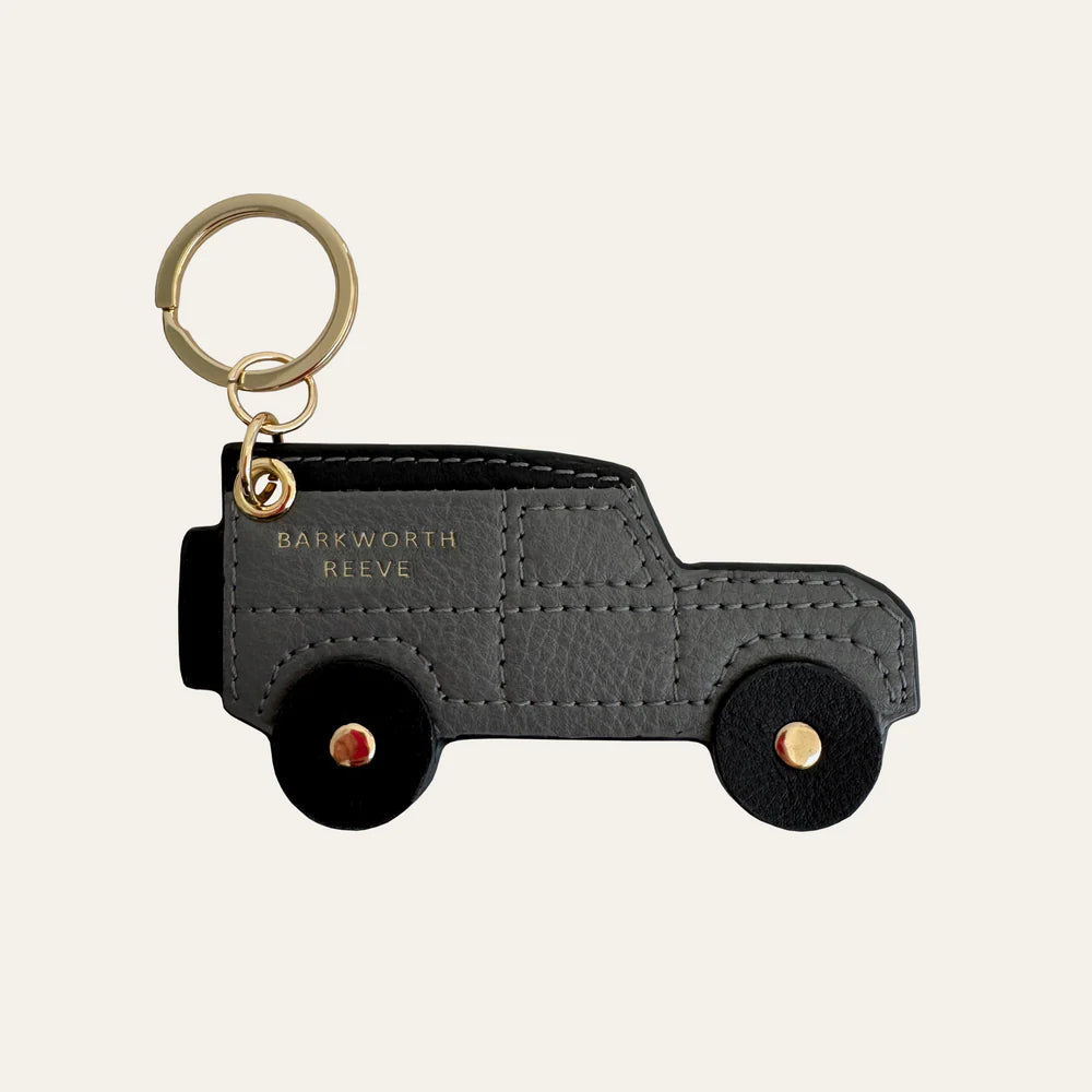 Black leather truck-shaped keychain with gold accents on a beige background