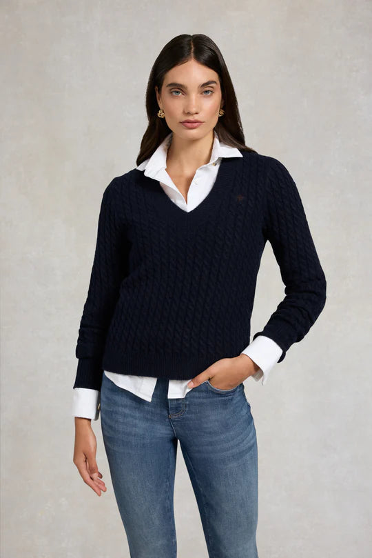 Woman wearing a navy sweater over a white shirt with blue jeans on a plain background
