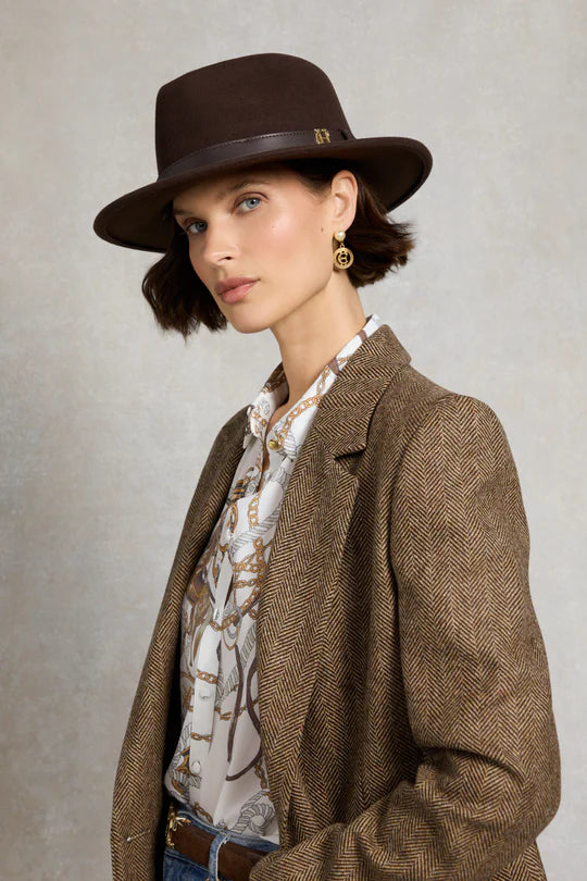 Woman wearing a brown fedora and herringbone jacket against a neutral background