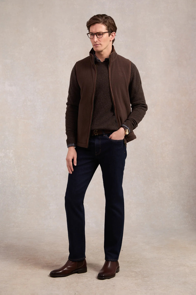 Man wearing a brown jacket, shirt, and jeans standing against a plain background