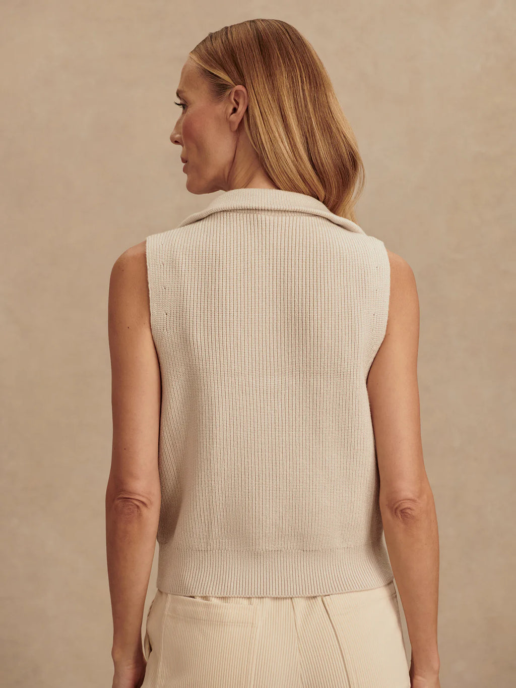 Woman wearing a beige ribbed knit vest against a beige background