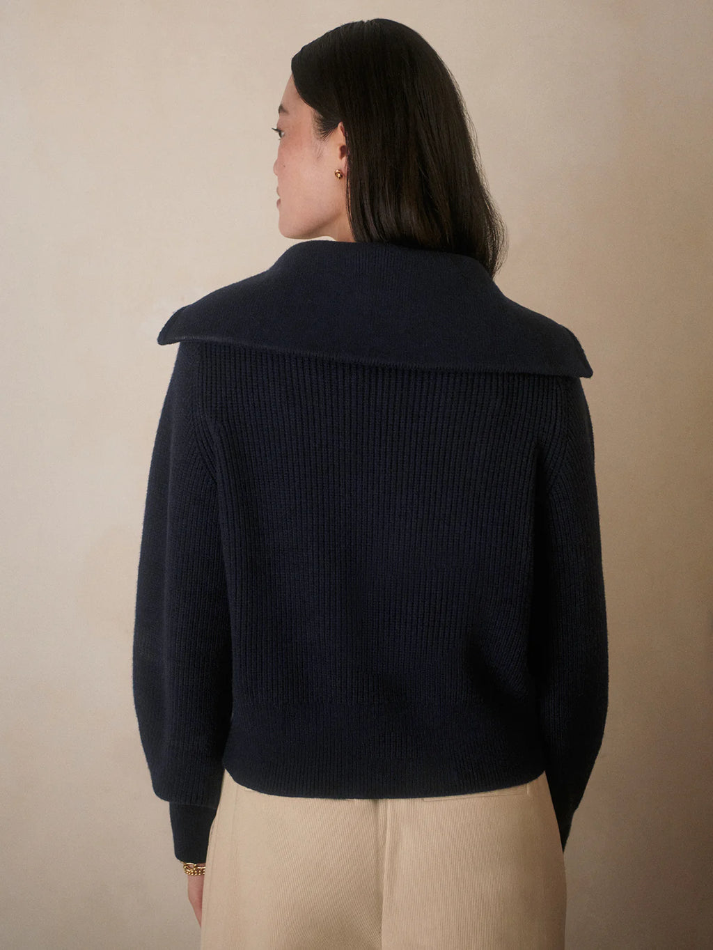 Person wearing a navy ribbed sweater with a high collar against a beige background