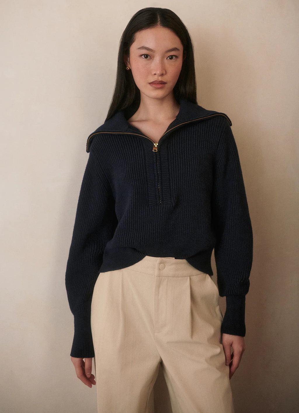 Person wearing a navy ribbed sweater with a high collar against a beige background