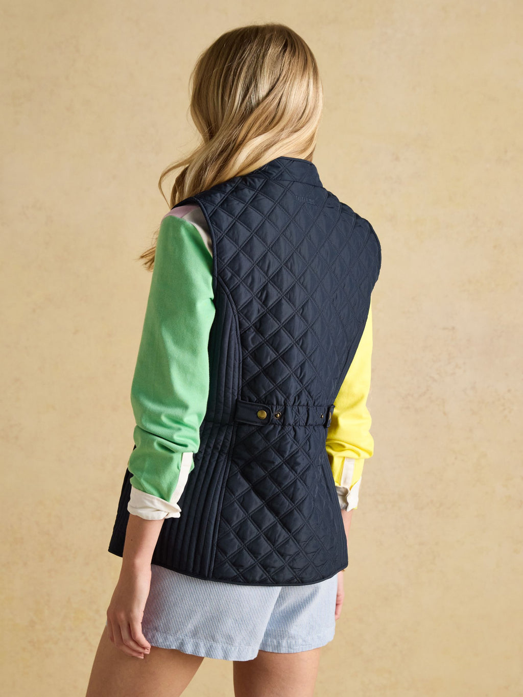 Person wearing a navy quilted vest over a green and yellow outfit on a beige background
