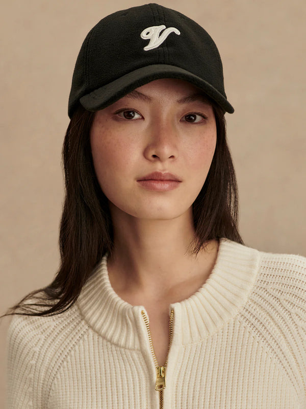 Woman wearing a black cap with a logo and a beige sweater against a beige background