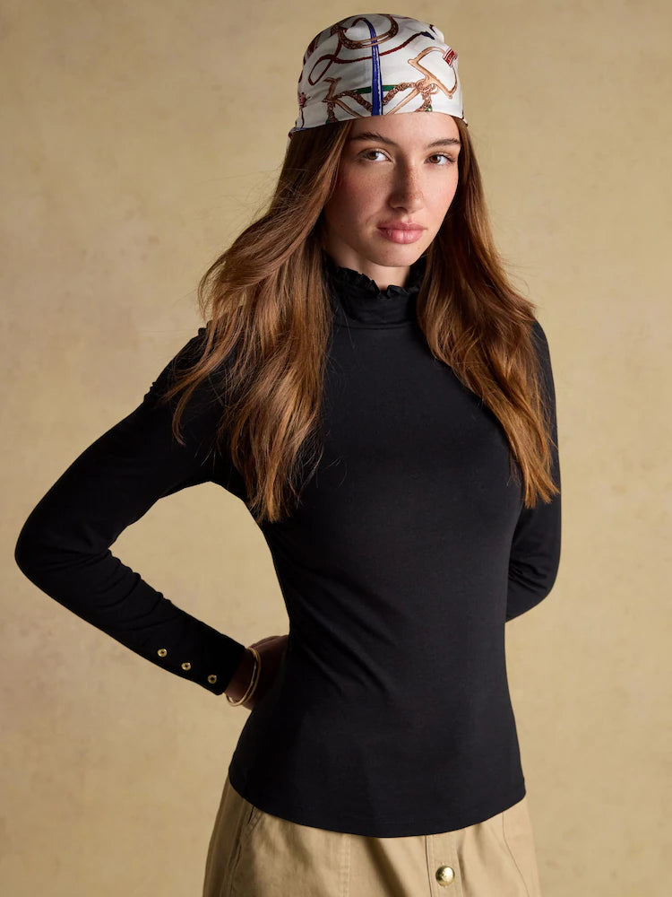 Woman wearing a black turtleneck and patterned headband against a beige background