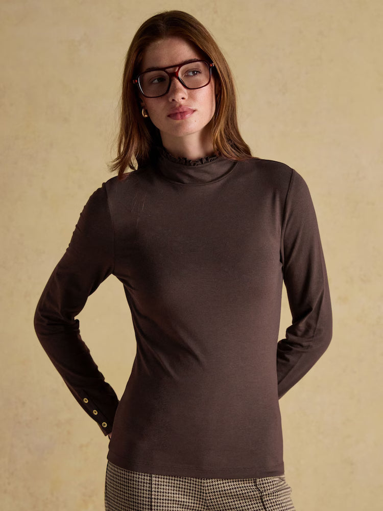 Woman wearing a brown turtleneck sweater against a beige background