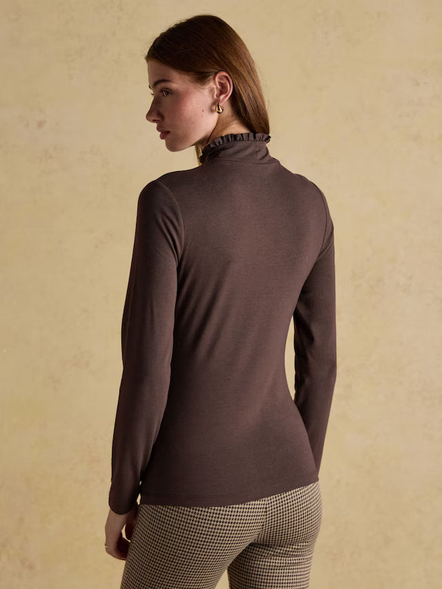Woman wearing a brown turtleneck sweater against a beige background