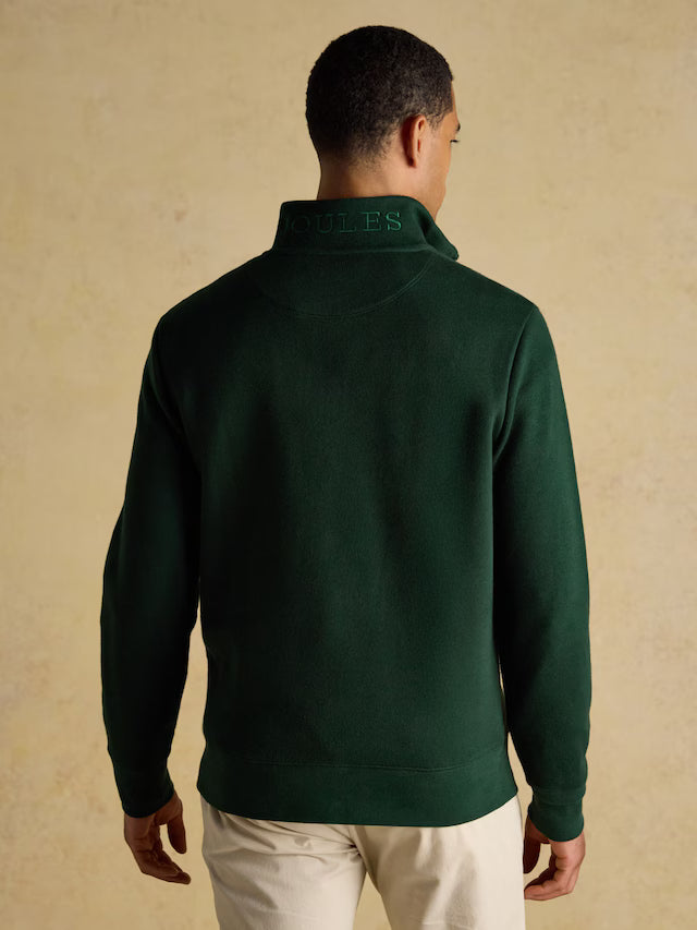 Man wearing a green half-zip sweater with 'Joules' branding on a beige background