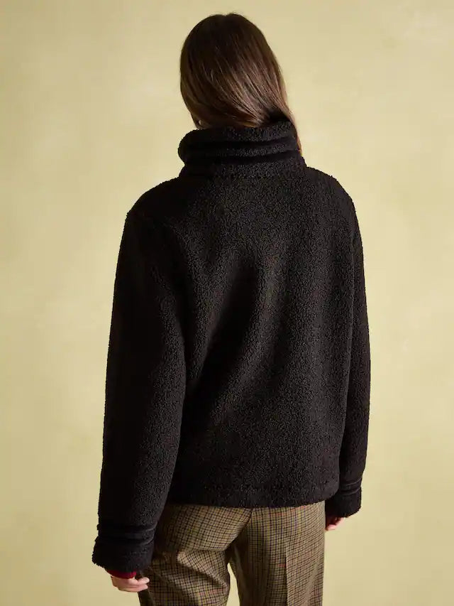 Person wearing a black turtleneck sweater against a beige background