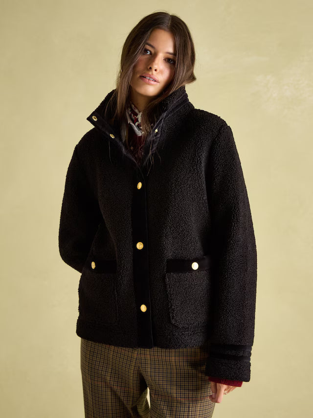 Woman wearing a black coat with gold buttons against a beige background