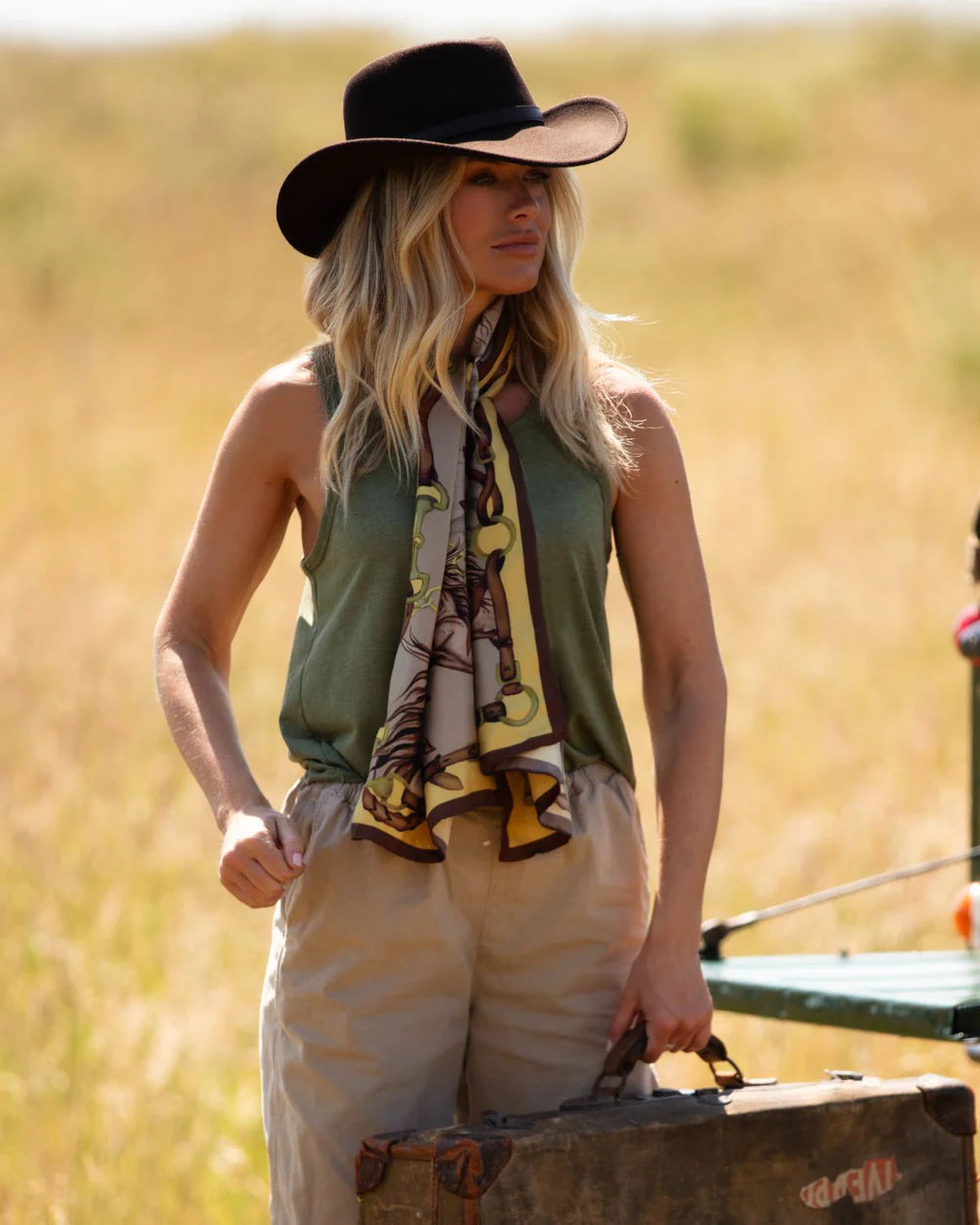 Woman in a safari outfit with a hat and scarf, standing in a grassy field.