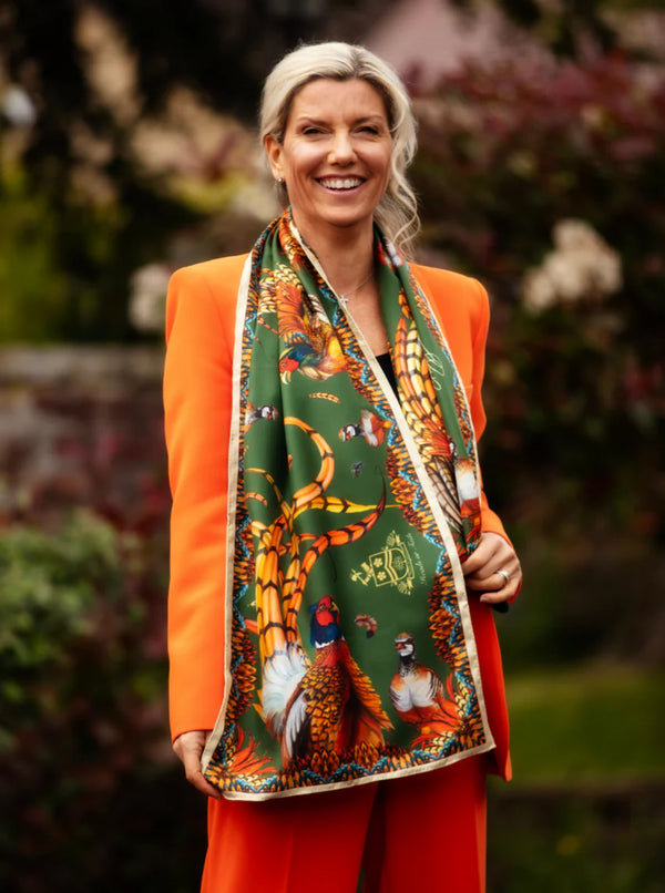 Woman wearing an orange jacket and red pants with a patterned scarf outdoors.