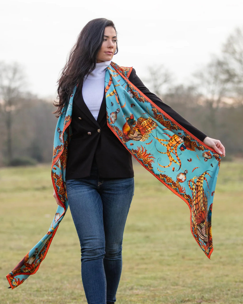 Woman holding a large, colorful scarf with a pattern of tigers in an open field.