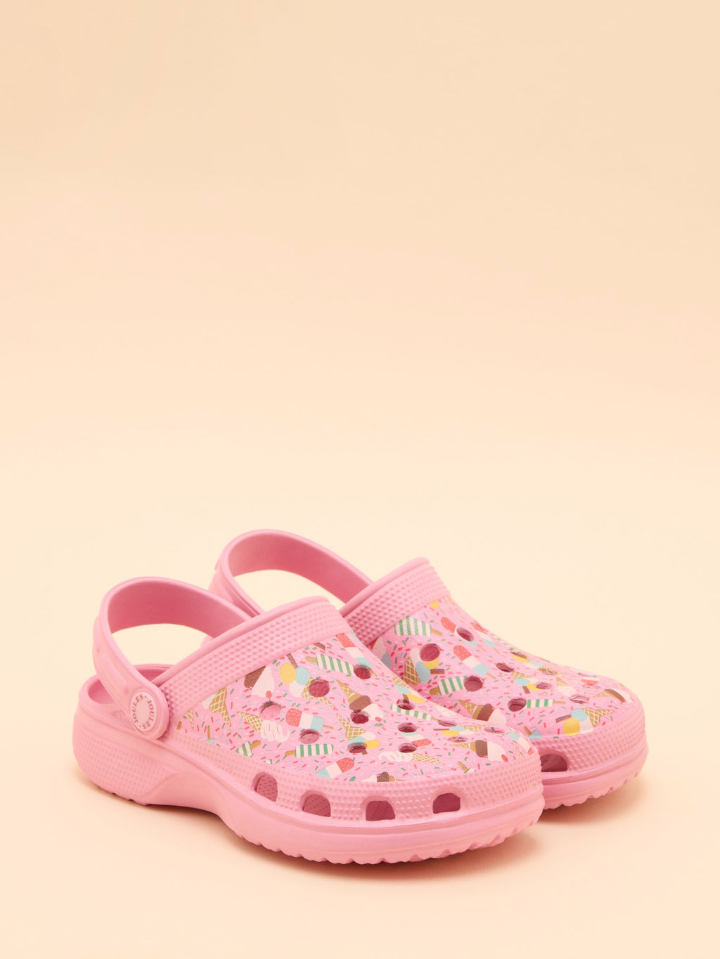 Pink children's clogs with colorful patterns on a beige background
