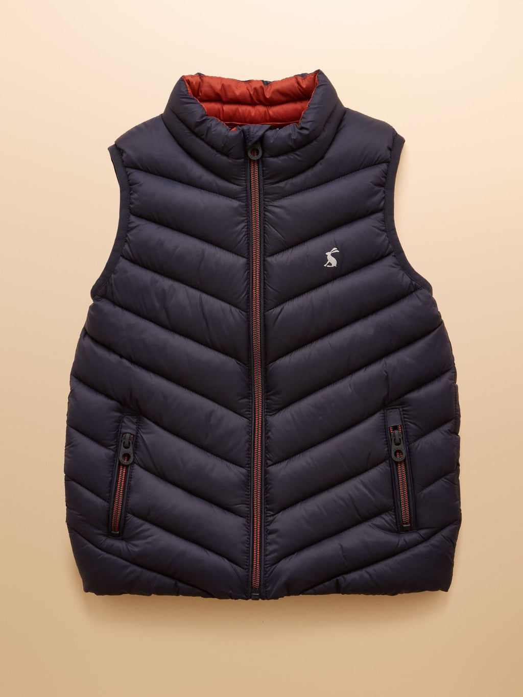 Navy puffer vest with red interior lining on a beige background