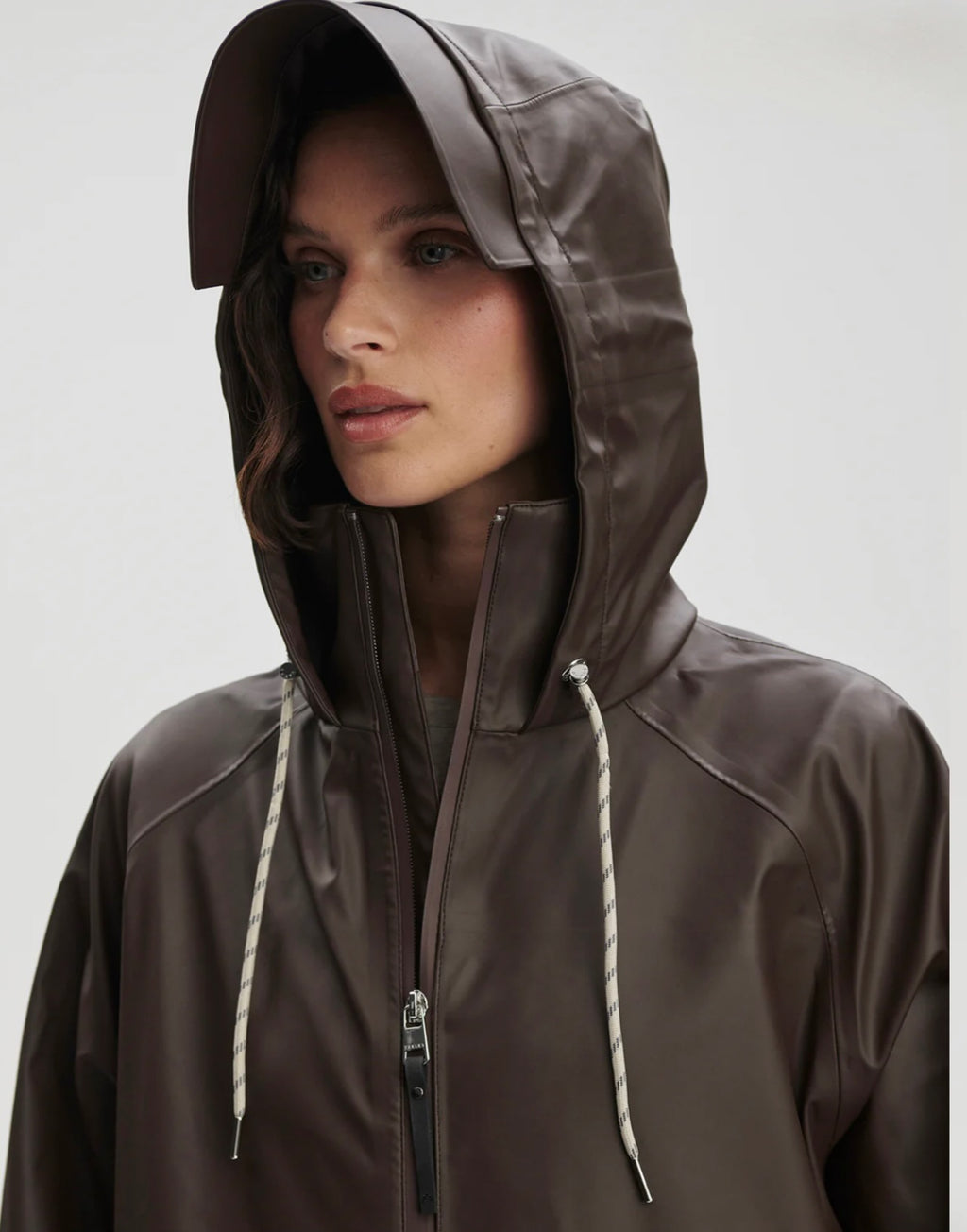 Person wearing a brown raincoat with a hood on a plain background