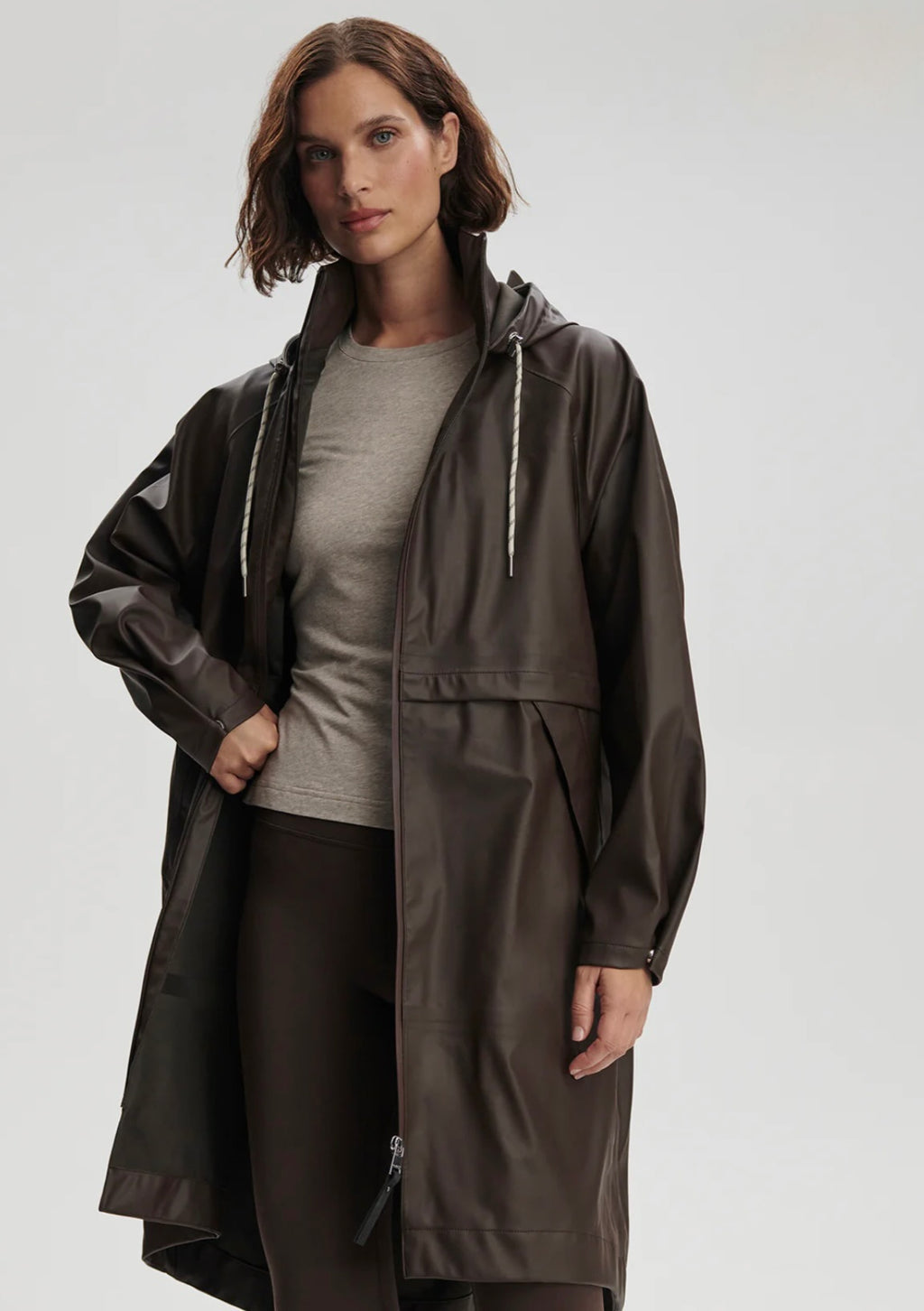 Woman wearing a long dark raincoat over a gray shirt on a white background