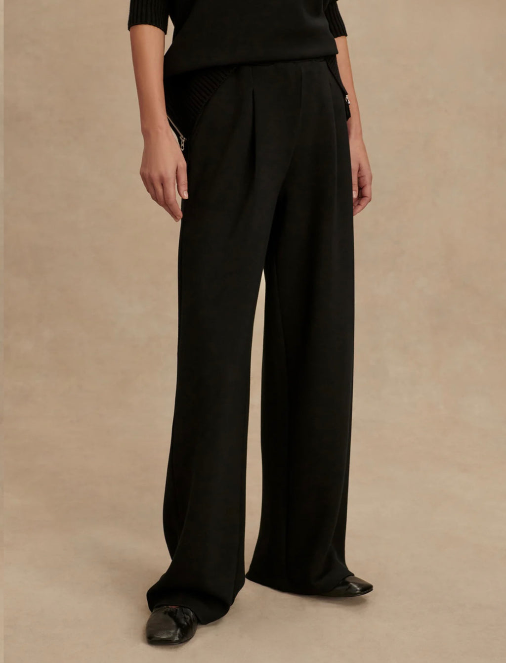 Person wearing black wide-leg pants on a beige background
