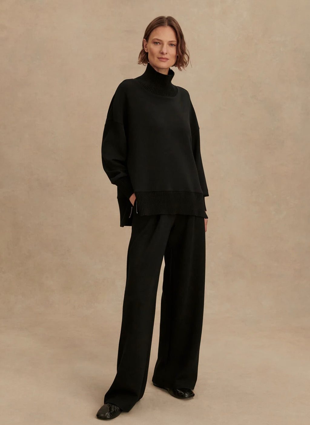 Person wearing a black outfit against a beige background