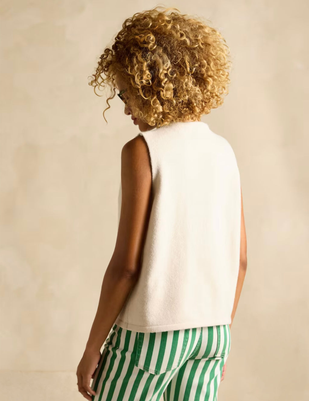 Person wearing a white sleeveless top and green striped pants against a beige background