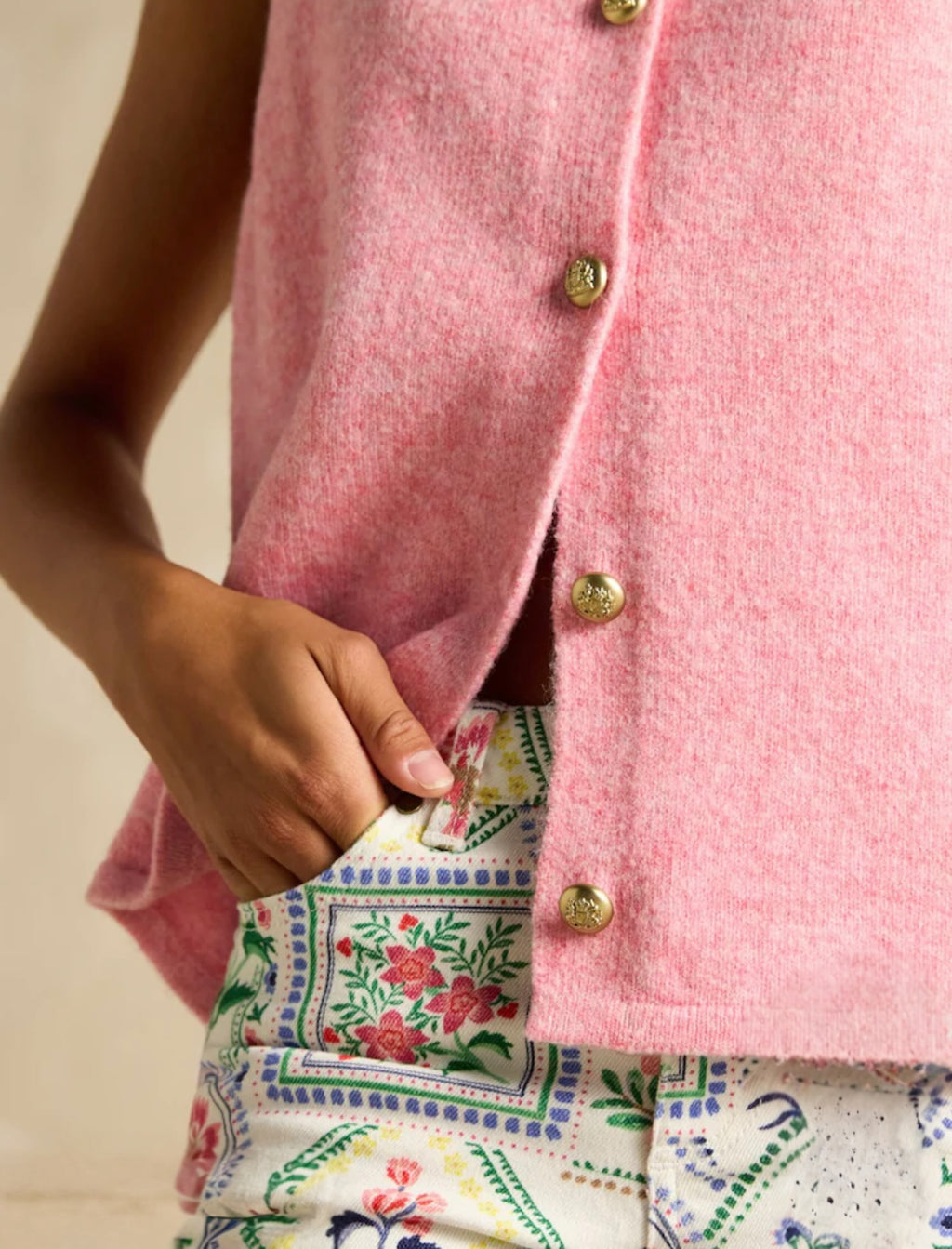 Close-up of a pink cardigan with gold buttons worn over a floral dress.