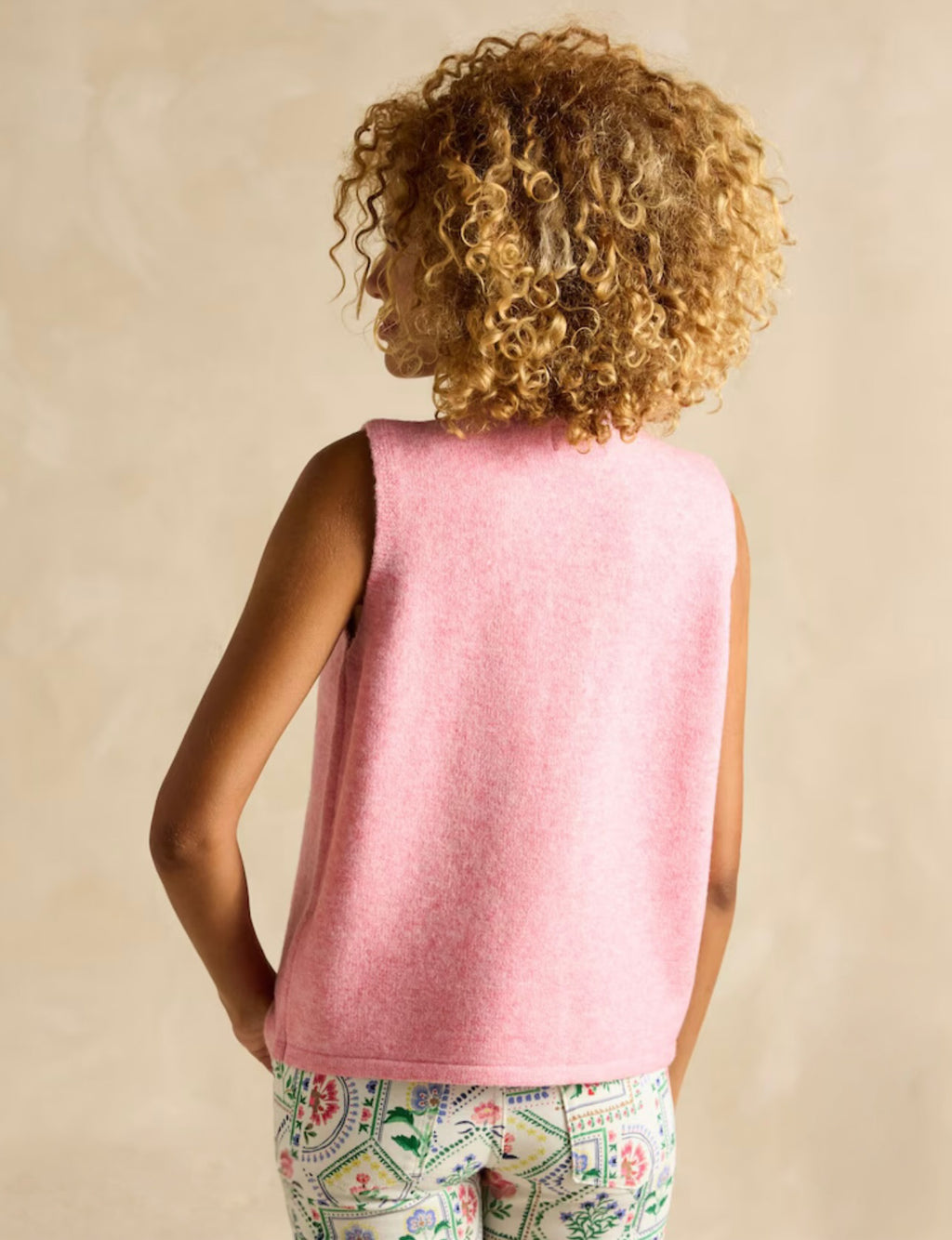 Person wearing a pink sleeveless top with a beige background