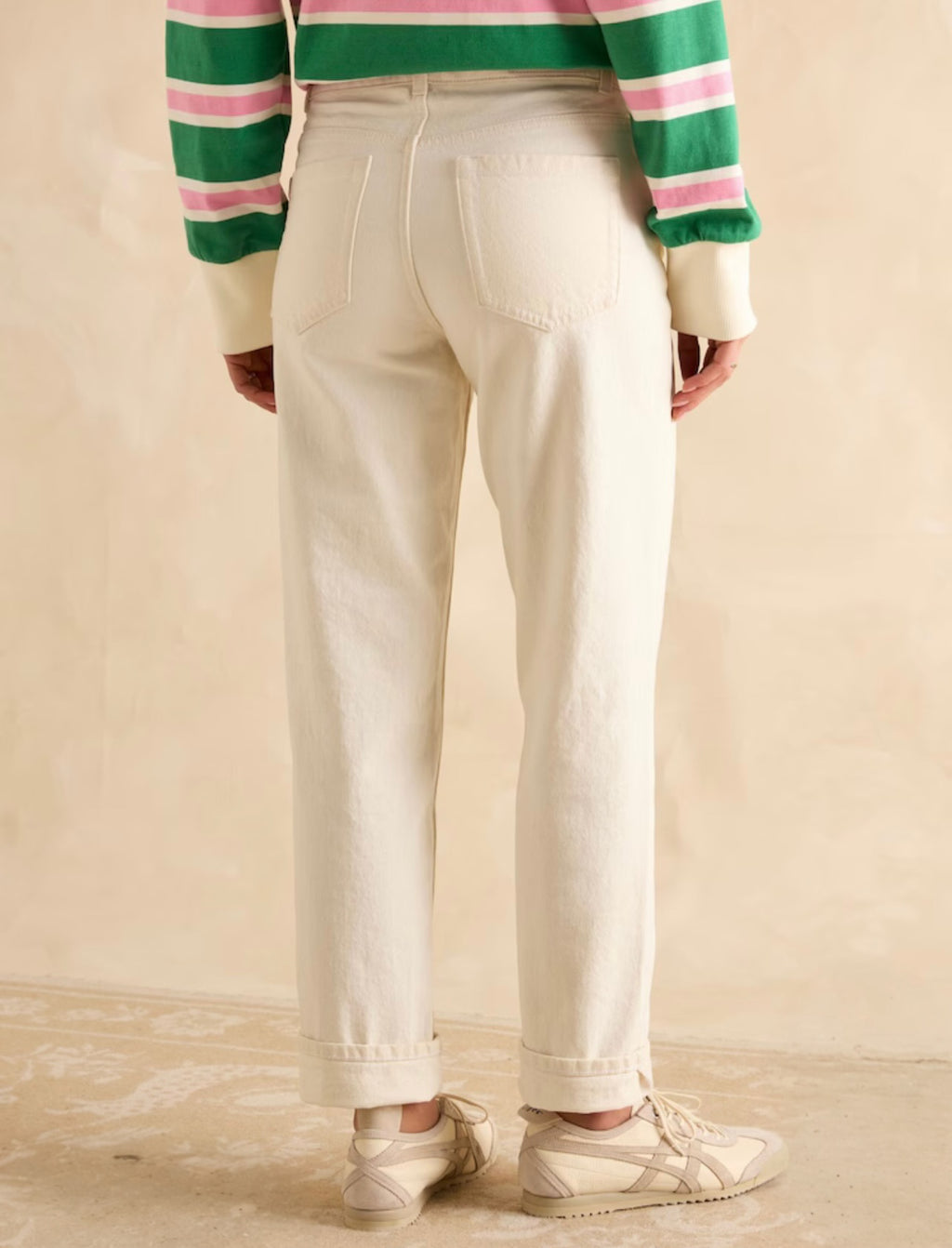 Person wearing a striped sweater and white pants on a beige background