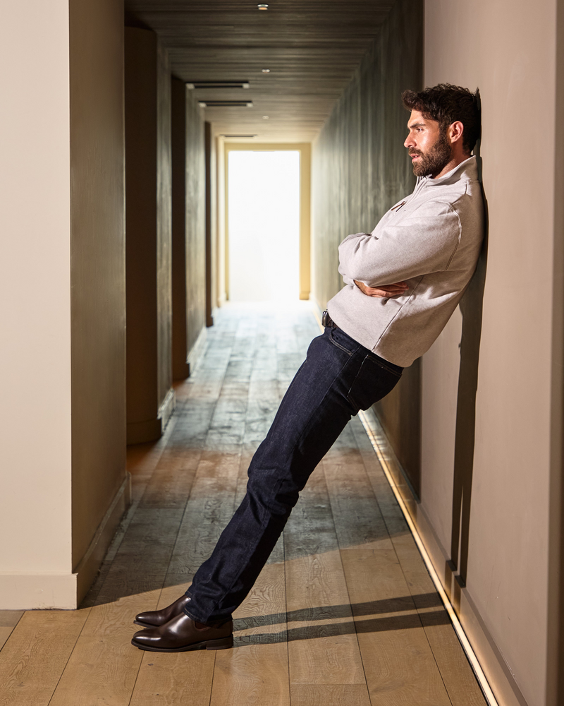 Man leaning against a wall in a hallway with light at the end