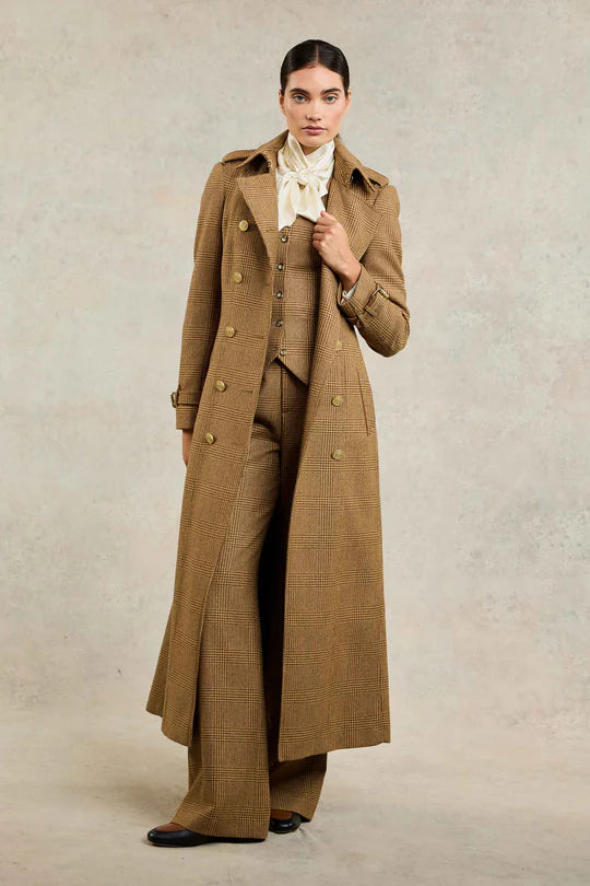 Woman wearing a long brown coat and pants against a plain background