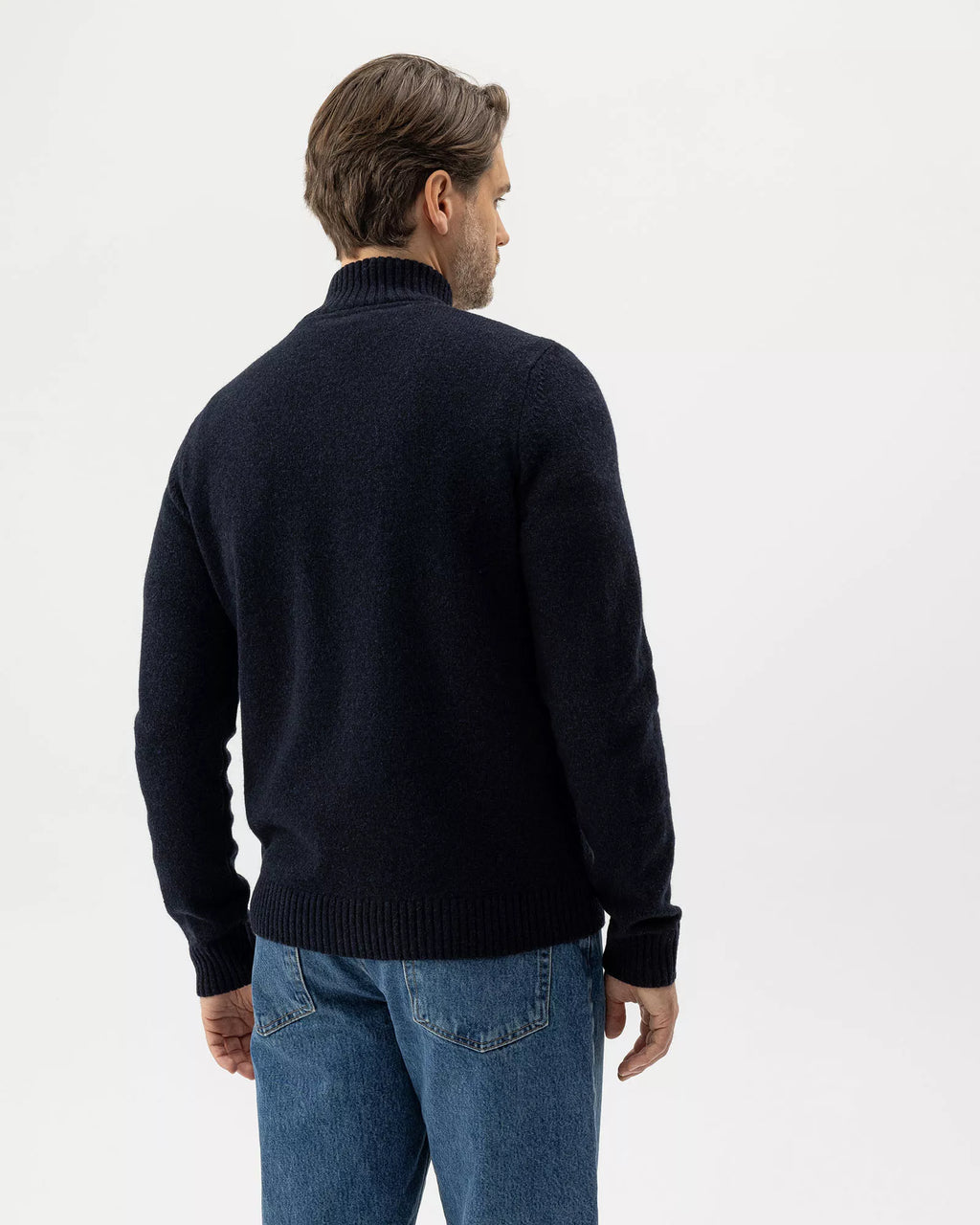 Man wearing a black sweater and blue jeans on a white background