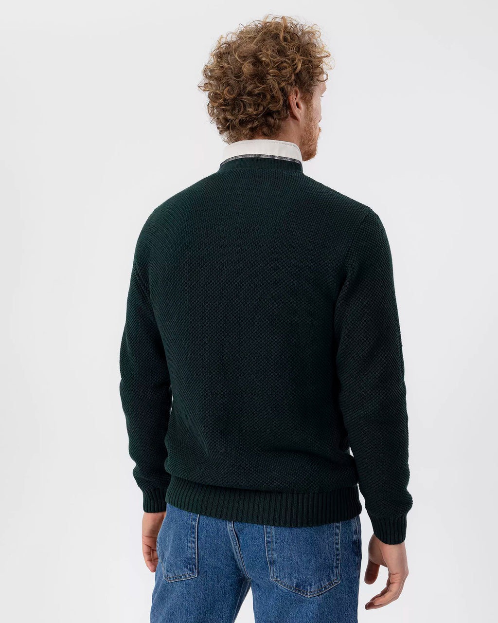 Man wearing a dark green sweater and blue jeans on a white background