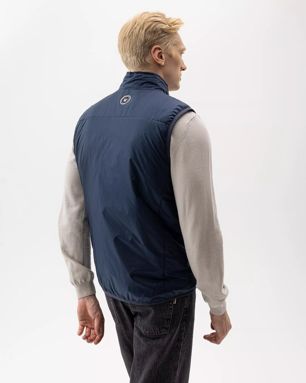 Man wearing a blue vest over a light gray shirt on a white background