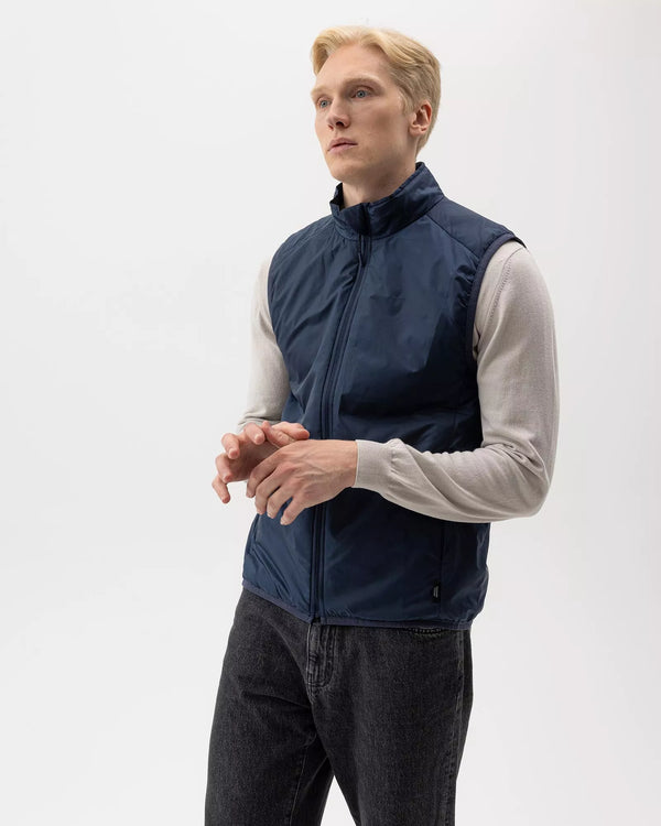 Man wearing a navy blue vest over a light gray shirt on a white background