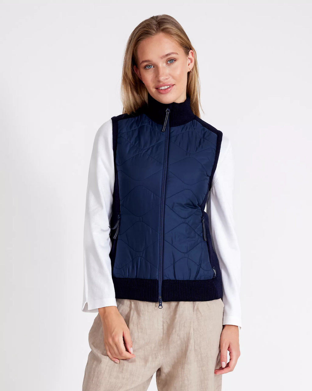 Woman wearing a navy blue quilted vest over a white shirt on a white background