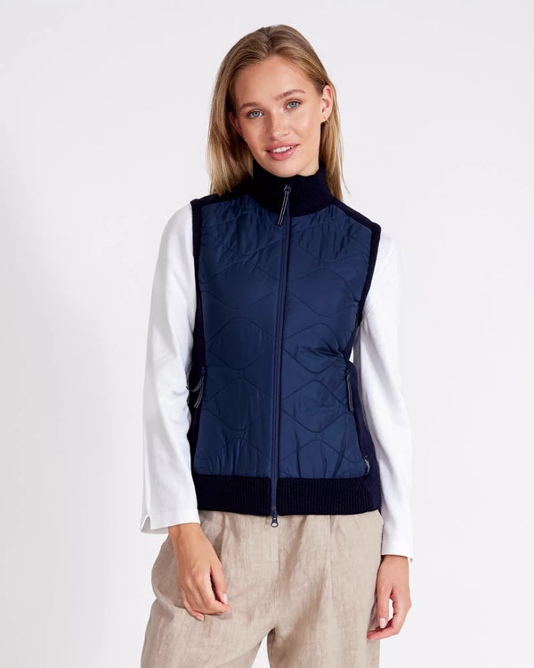 Woman wearing a navy blue quilted vest over a white shirt on a white background