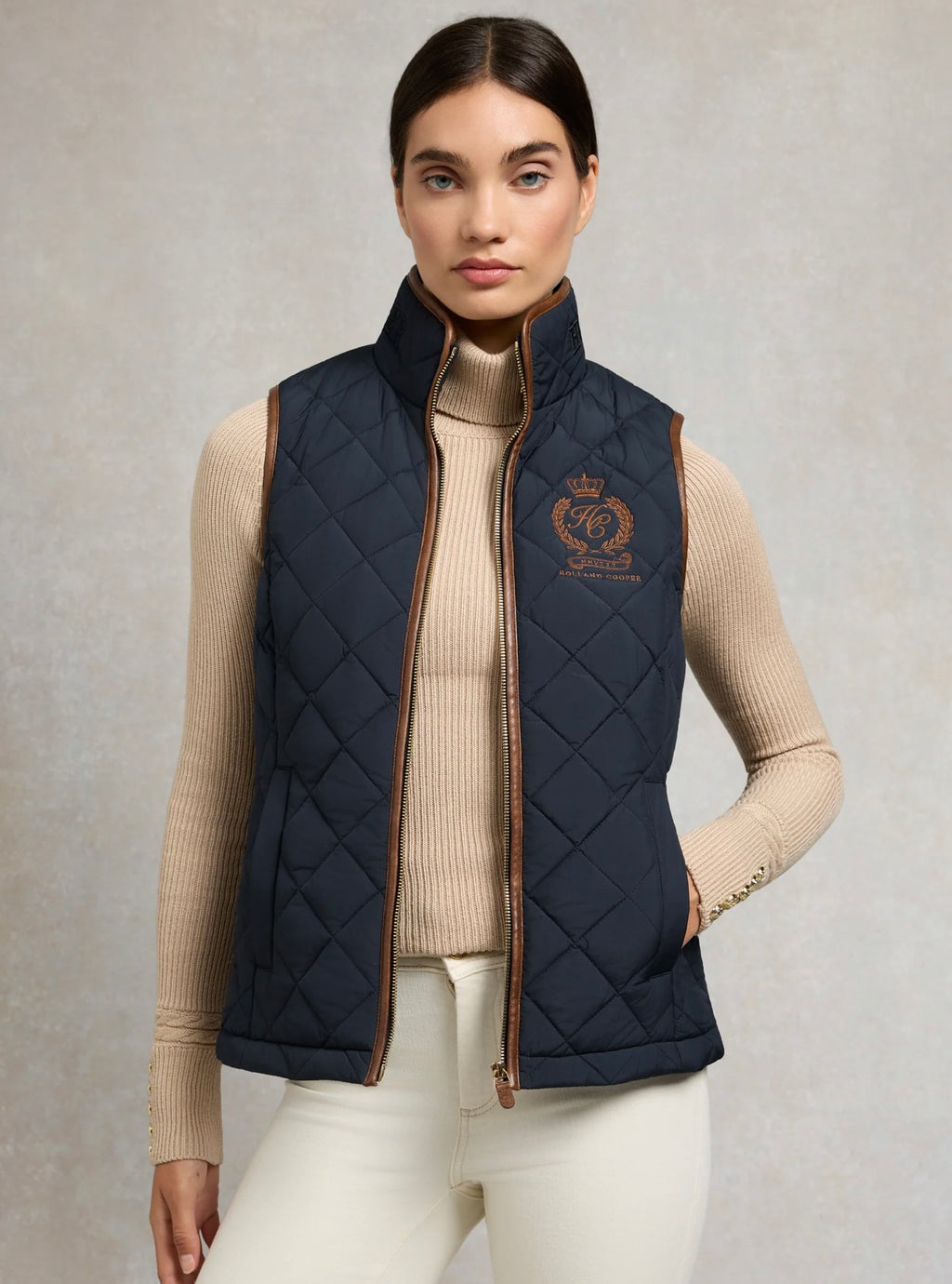 Woman wearing a navy quilted vest with a brand logo on a neutral background