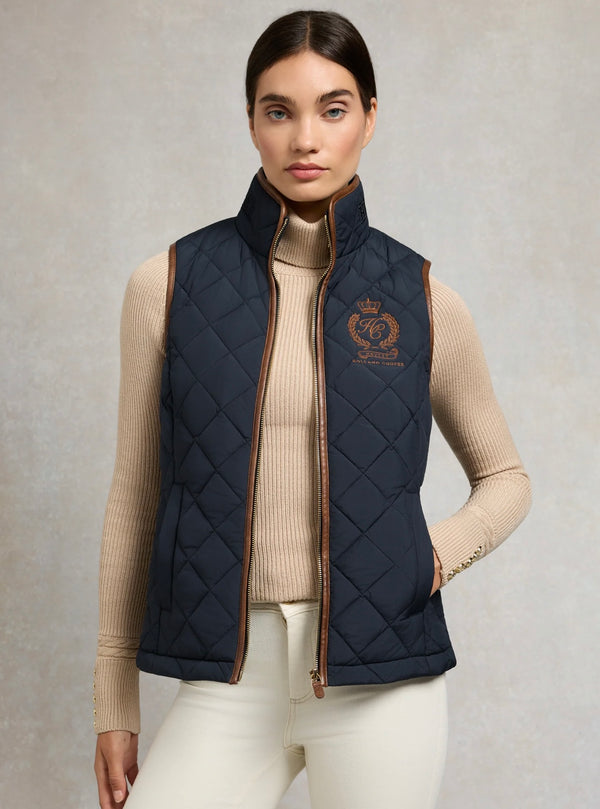 Woman wearing a navy quilted vest with a brand logo on a neutral background