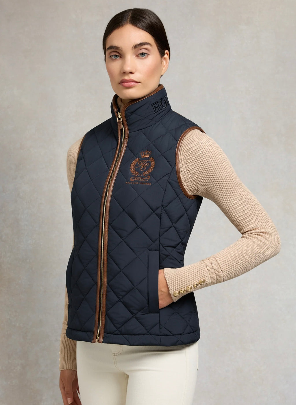 Woman wearing a navy quilted vest with a brand logo on a neutral background